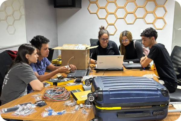 Vários jovens estão envolvidos em atividades; dois estão manipulando sensores, enquanto três estão concentrados em um notebook.