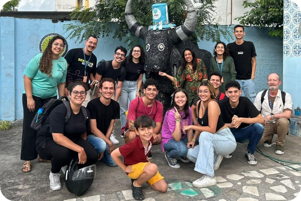 Um grupo de pessoas sorrindo e posando para fotos ao redor de uma escultura de boi.